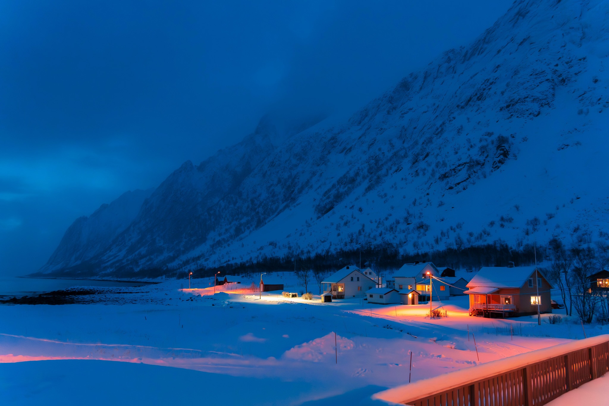 Snowy mountain village at dusk with illuminated cabins and winter landscape in Europe