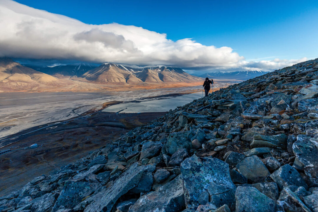Women hiking on rocky ridge with Arctic mountains and glacier valley in Svalbard summer wilderness expedition