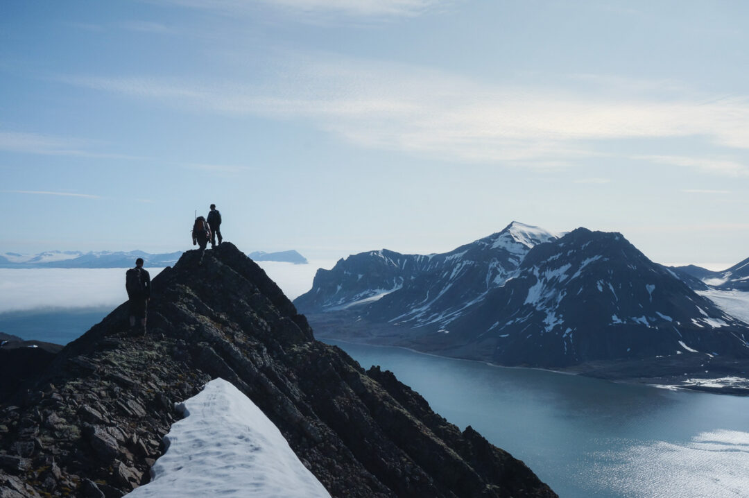 Hikers on a snowy mountain ridge overlooking Arctic fjord and glaciers in Svalbard, summer expedition