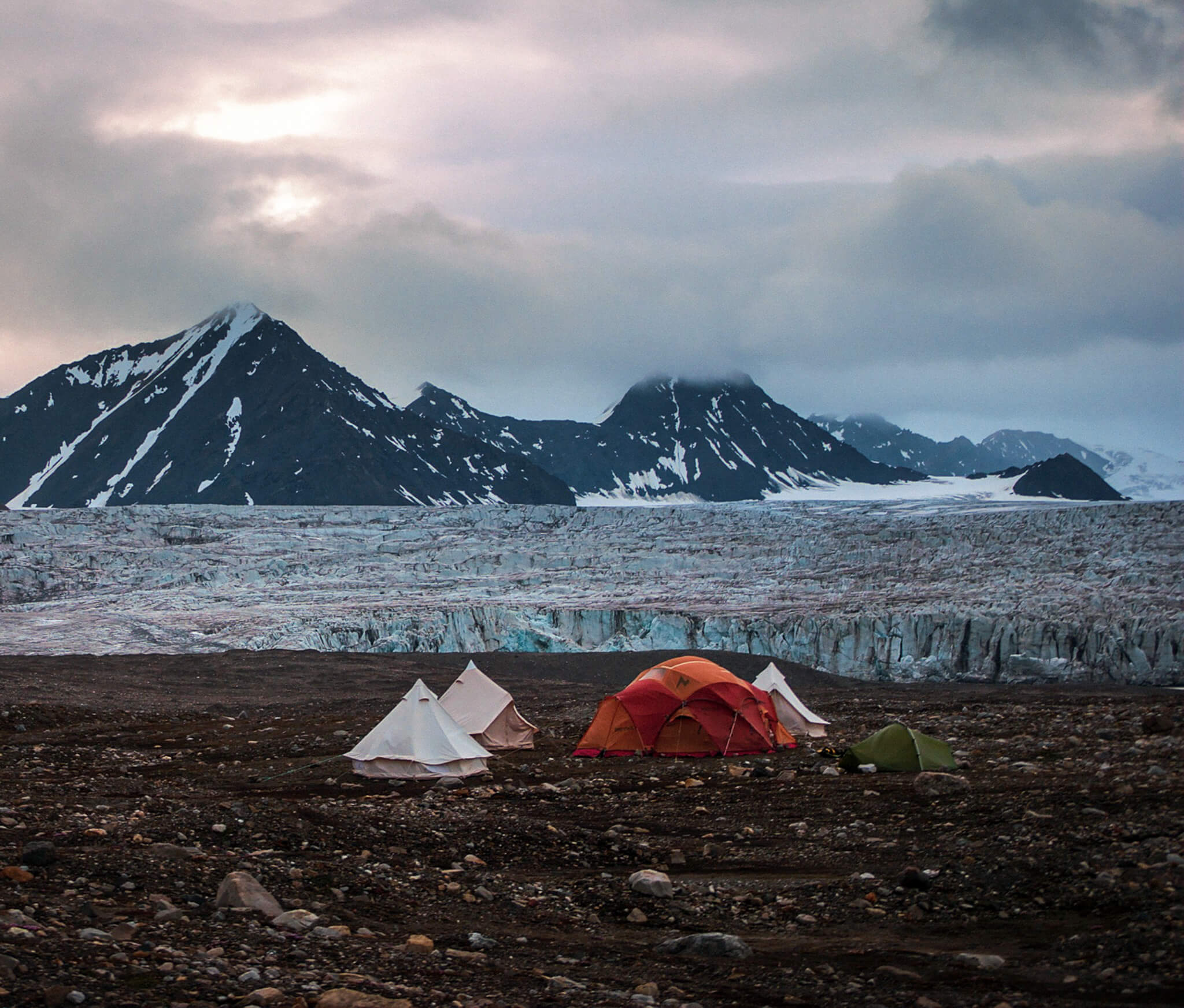 Camping tents on a glacier plain in Svalbard with snowy mountains and Arctic wilderness landscape