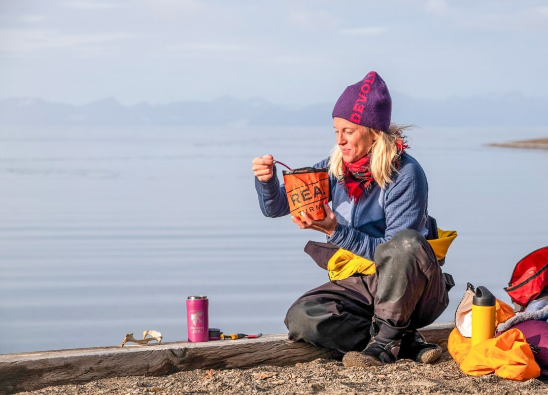 Women on a summer expedition in Svalbard, packing gear on a rocky Arctic shore