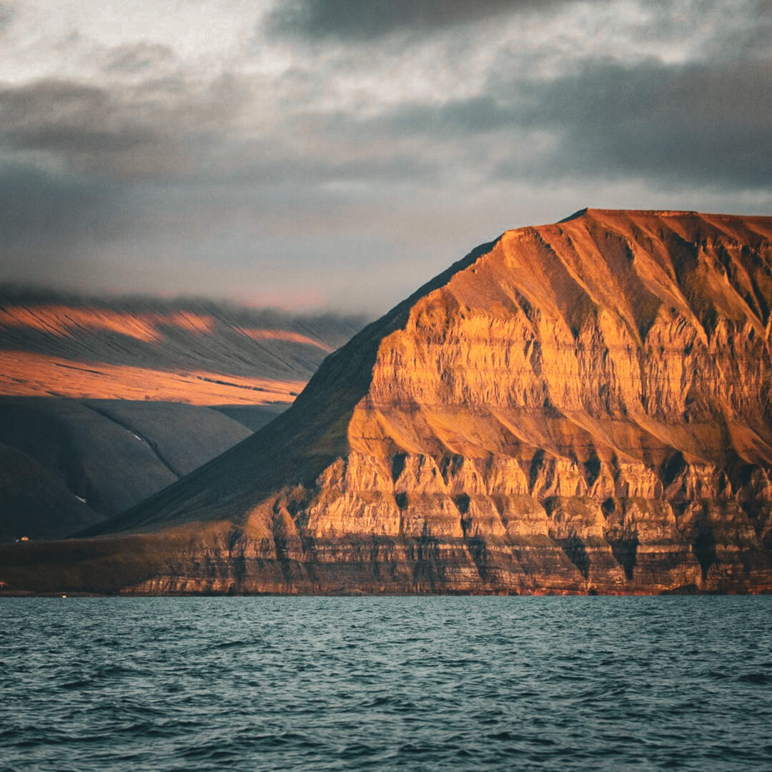 Arctic coastline with rocky cliffs and sea in Svalbard, Norway at summer dusk