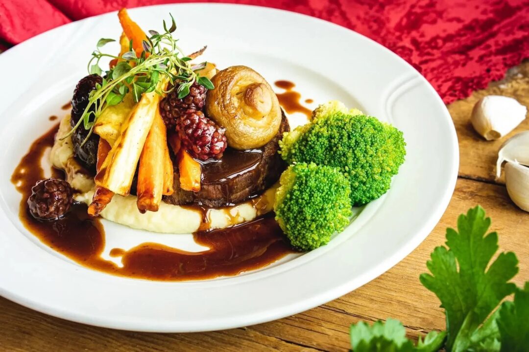 Roasted meat with vegetables and herbs served on a white plate with red wine-style sauce