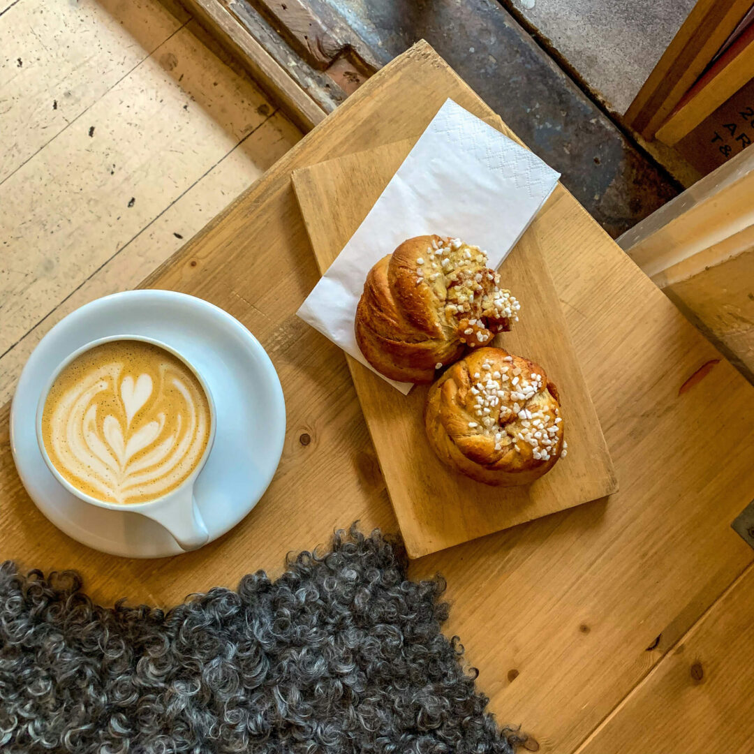 Two sesame-topped pastries on a wooden board beside a latte cup on a table