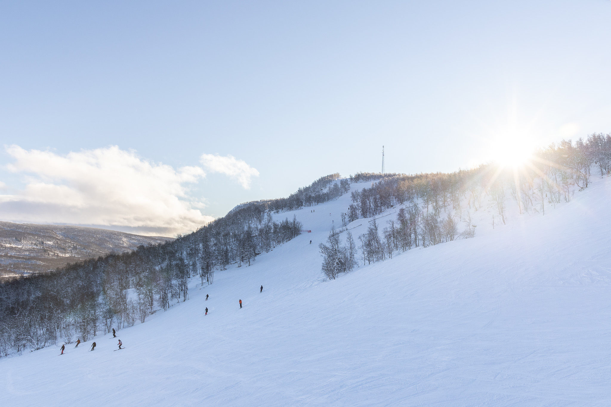 Snowy ski slope in winter mountains with skiers on the piste under a bright sun