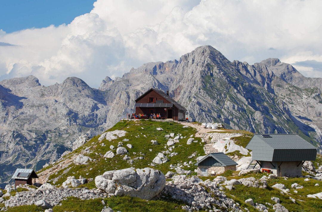 Mountain hiking huts on a grassy ridge in Slovenia’s Alps under rocky peaks
