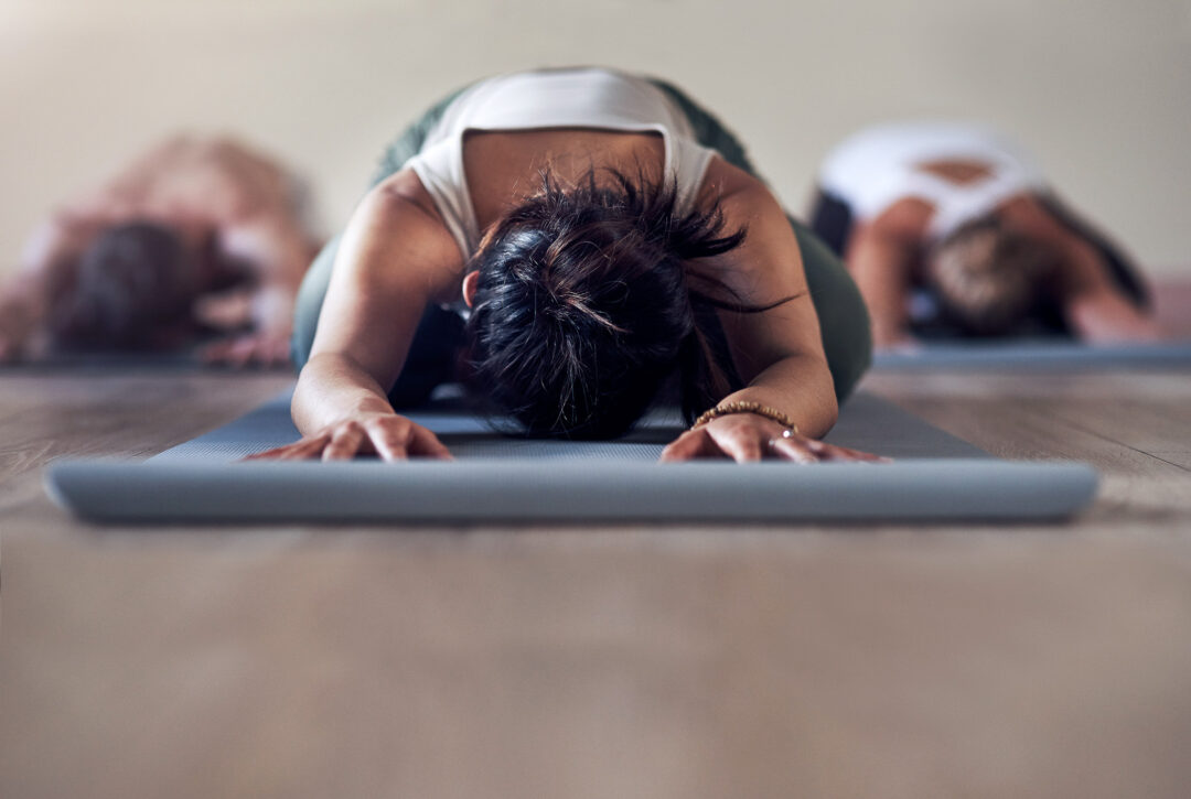 Women doing yoga in a studio, practising a forward-bend pose on mats.