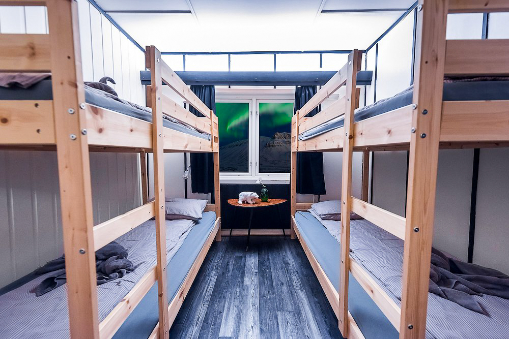 Wooden bunk beds inside a shared cabin with beds and a small table by the window