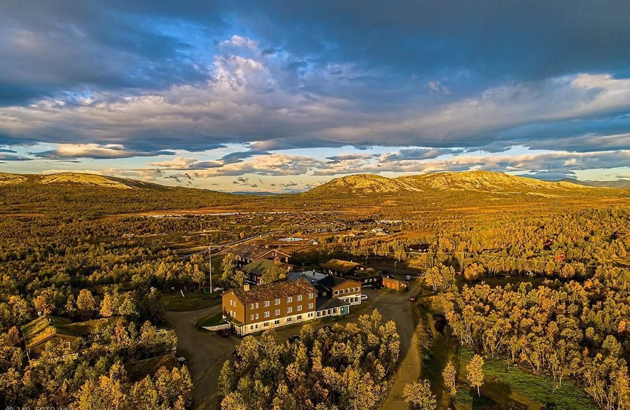 Countryside lodge surrounded by autumn trees under a cloudy sky, aerial view at golden hour