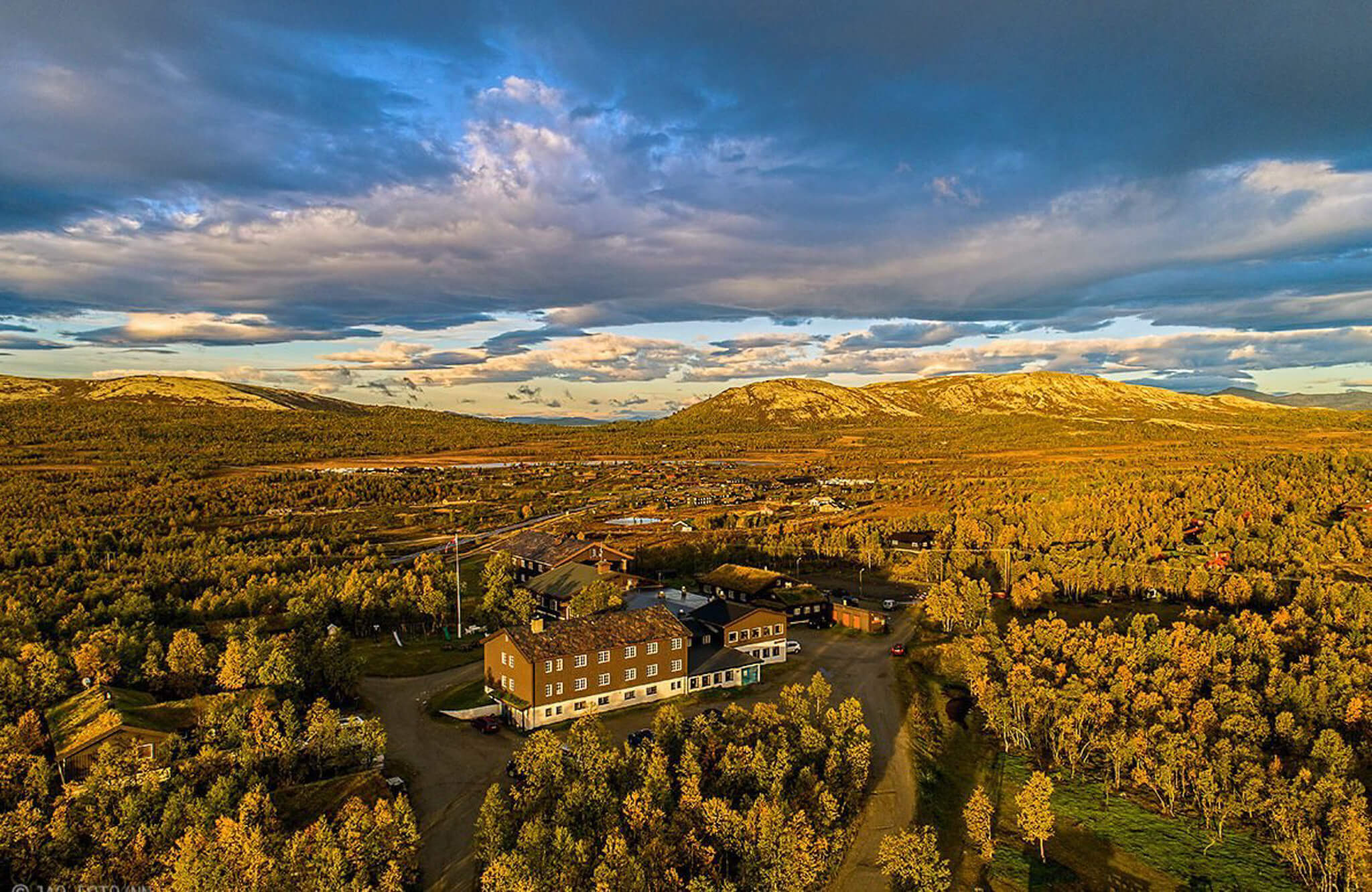 Aerial view of autumn valley in Norway with a lodge, winding road and forested hills