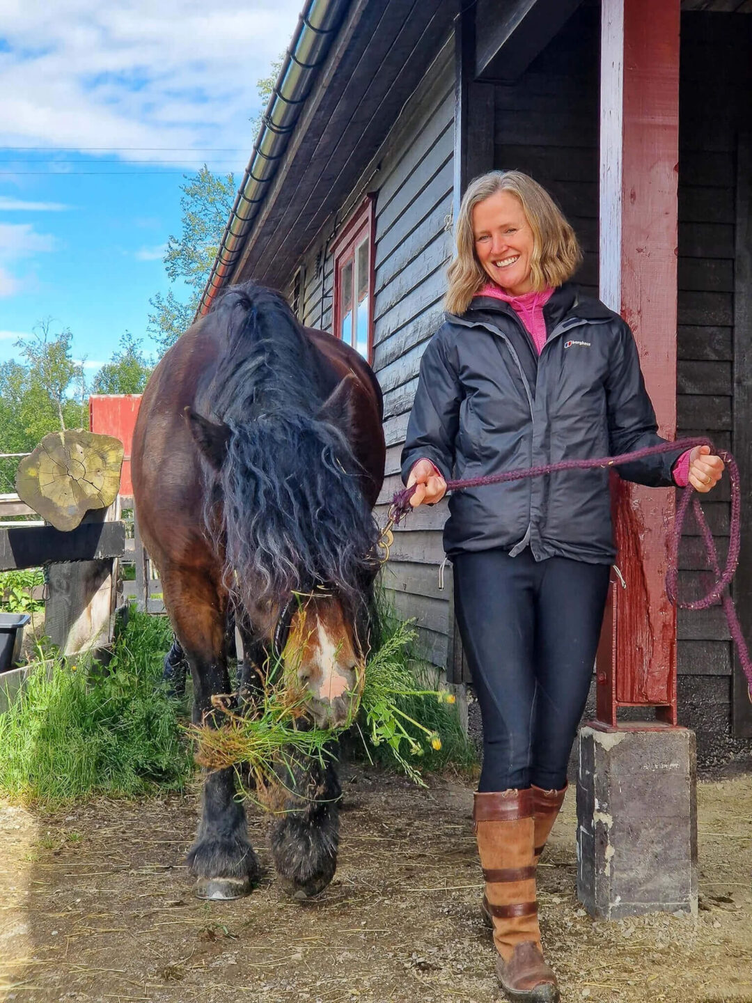 Woman leading a horse beside a stable doorway outdoors, horse riding holiday