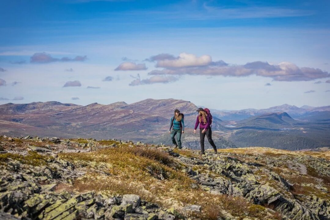 Two women trekking along a rocky mountain ridge with distant valleys and clouds in Scandinavia