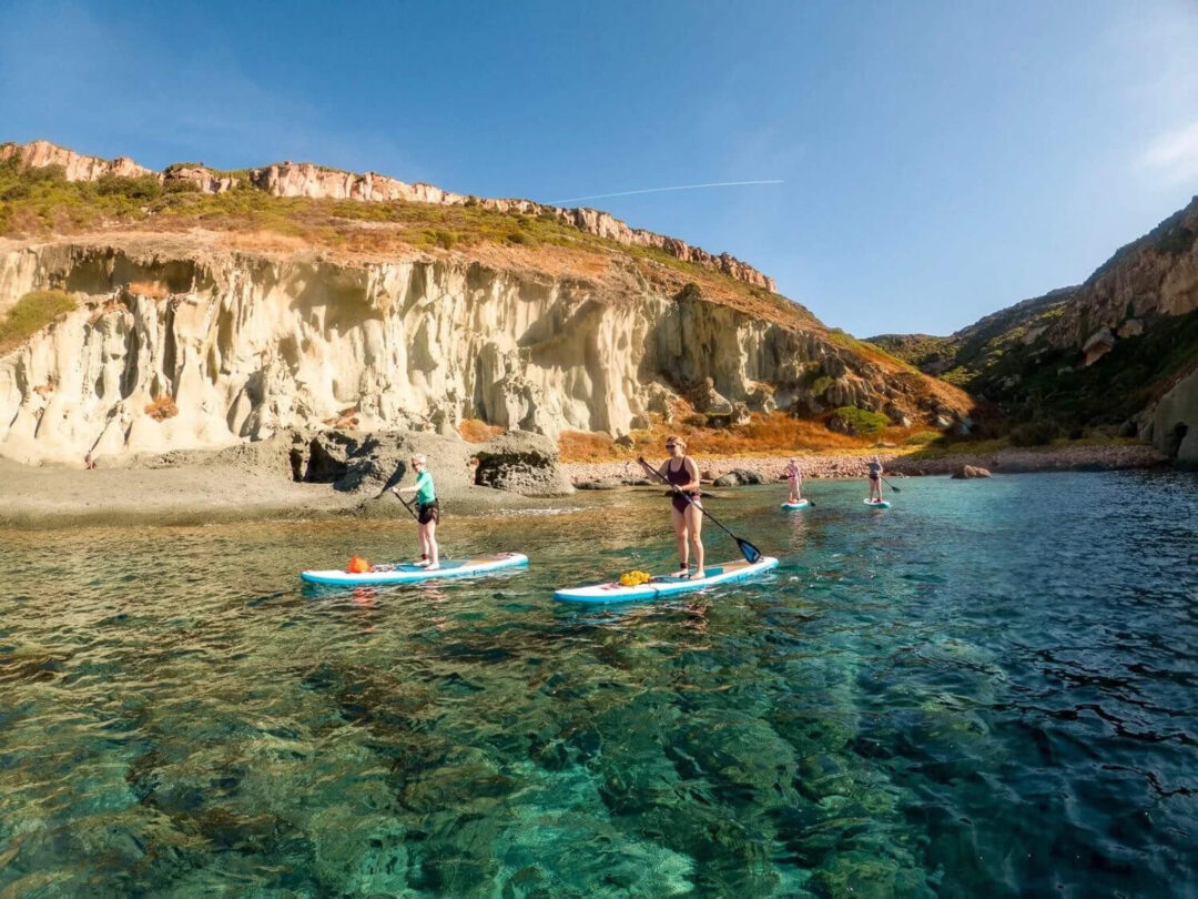 Women paddleboarding near rocky cliffs in Sardinia, SUP on clear sea water