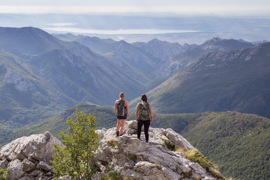 Two women hiking on a rocky mountain ridge with panoramic valley views