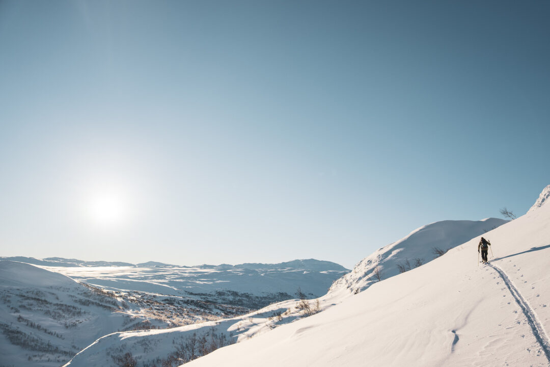 Cross-country skier gliding on snow-covered mountain tracks under a clear blue sky