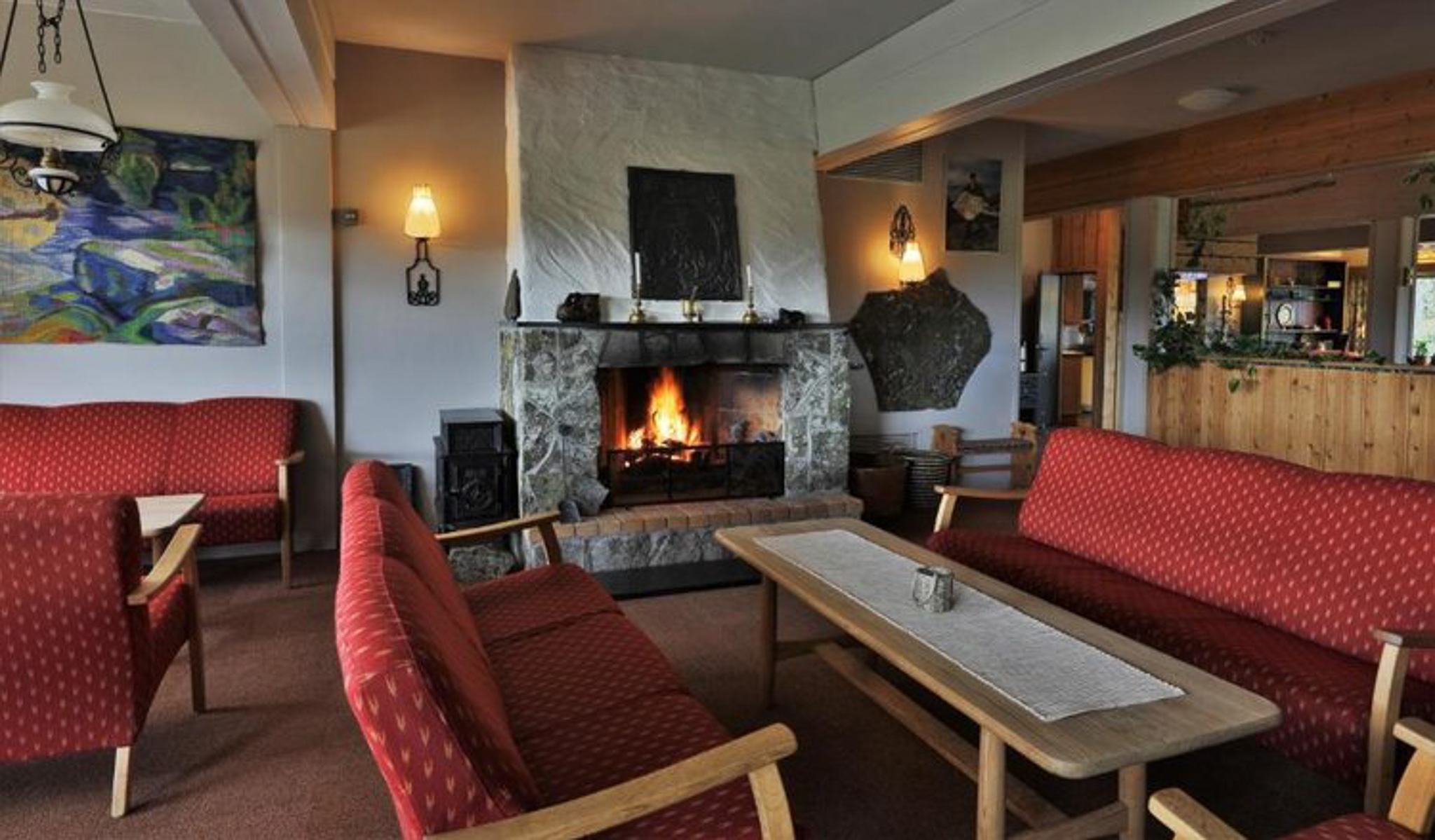 Cozy living room with stone fireplace, red seating and wooden walls indoors in a Norwegian lodge