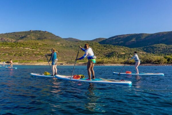 Women paddleboarding on a calm lake with green hills and mountains in the background