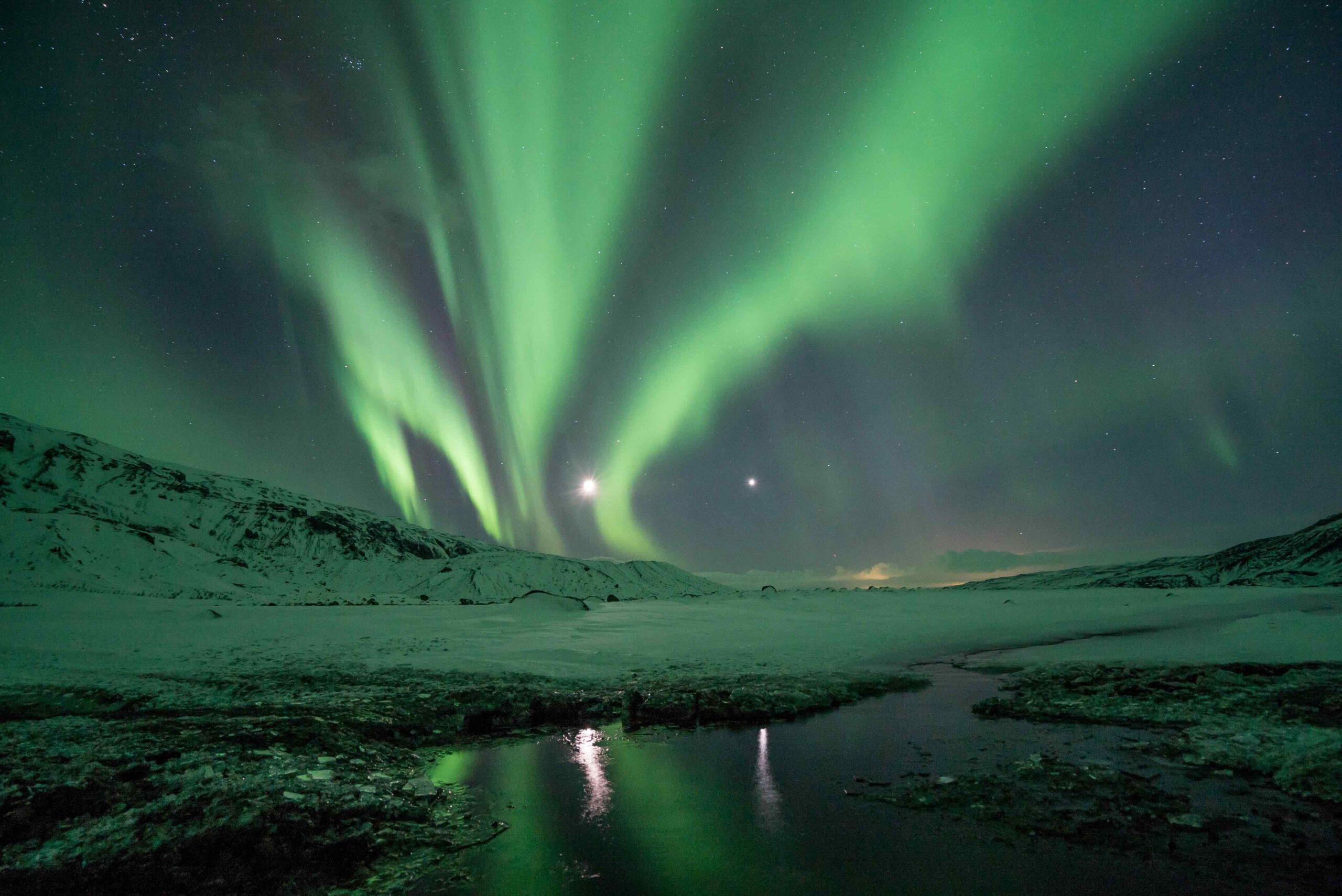 Northern lights over snowy landscape and water in iceland