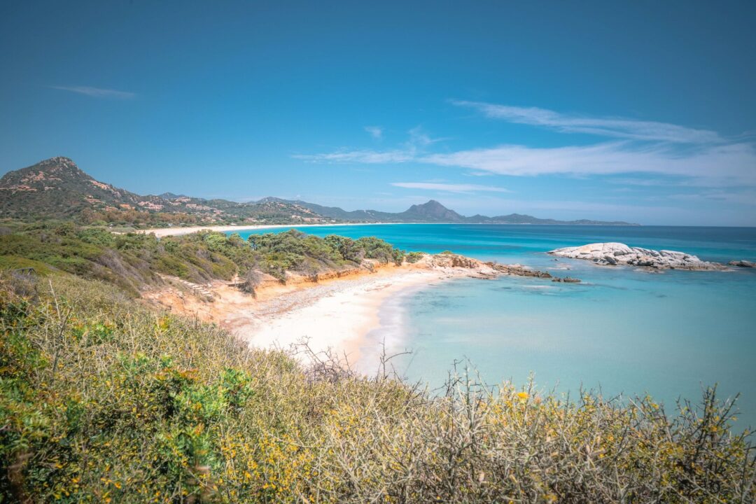 Sardinia coastline with sandy beach and turquoise sea, viewed from a coastal path through scrubland