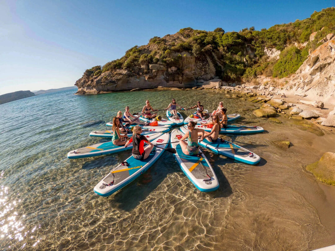 Women practising SUP on paddleboards in a sheltered cove, Sardinia