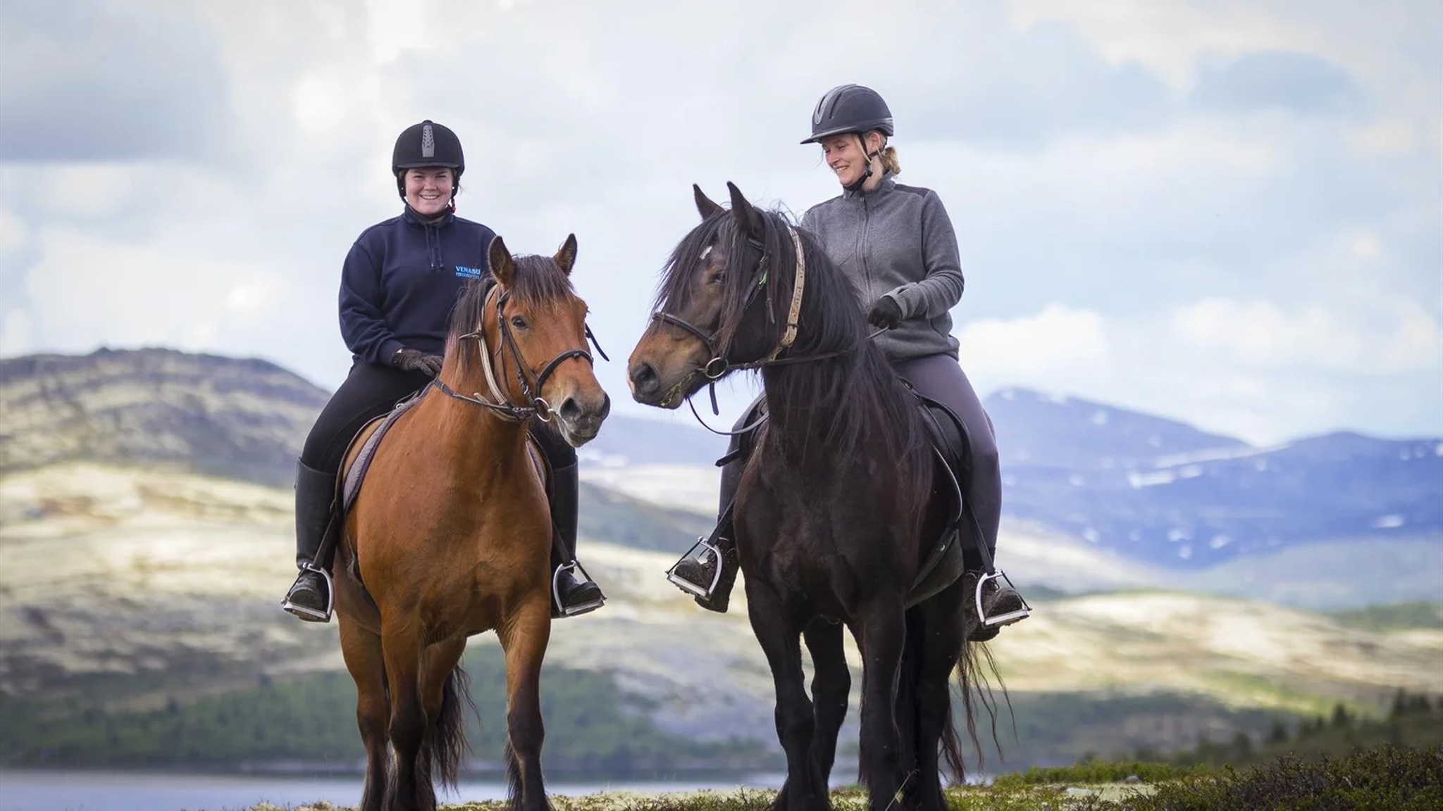 Women on horseback riding in Norway with mountain views.