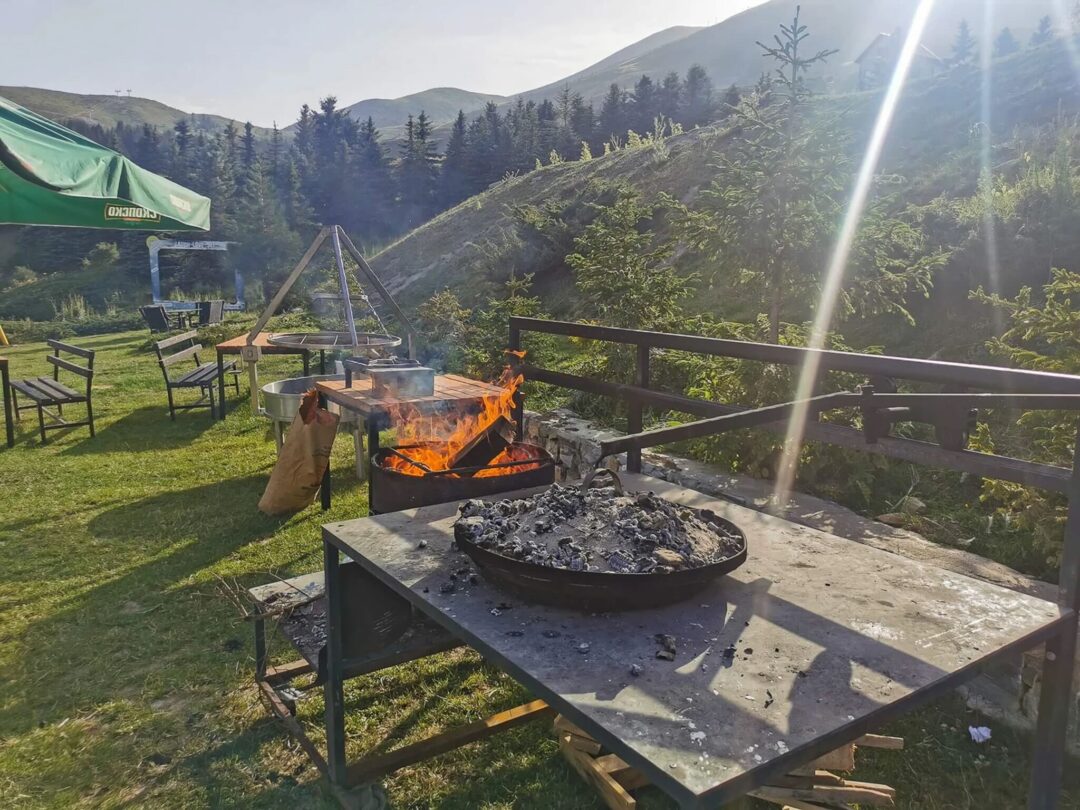 Outdoor campsite barbecue on a wooden terrace with tents and mountain valley views at golden hour
