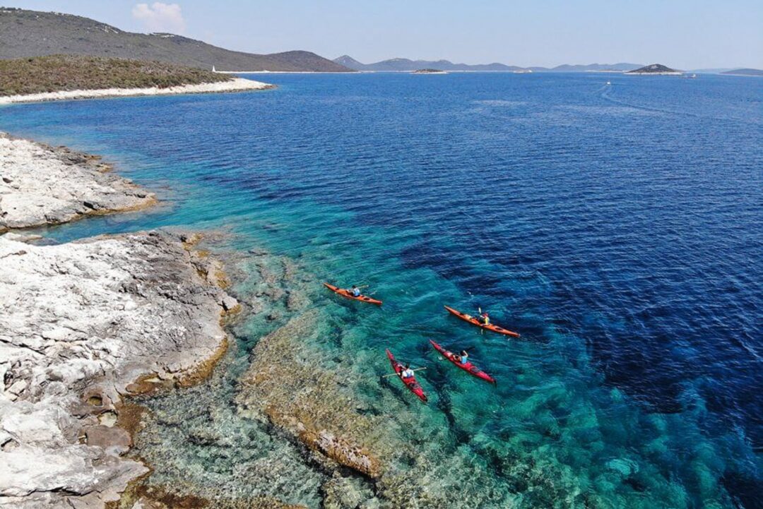Kayaks on clear blue sea near a rocky island coastline