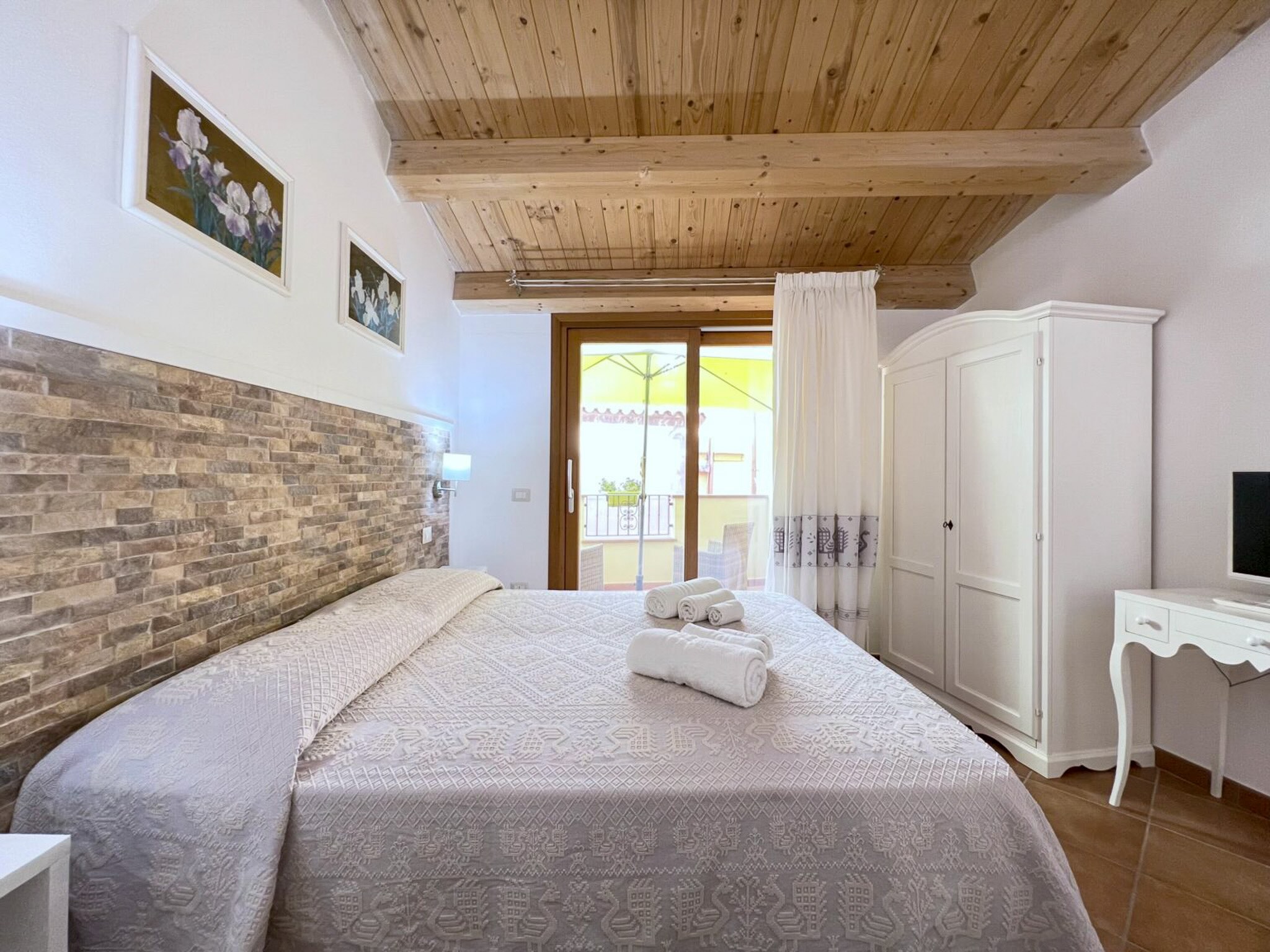 Bright bedroom interior with double bed, white wardrobe and wooden ceiling with open doorway window