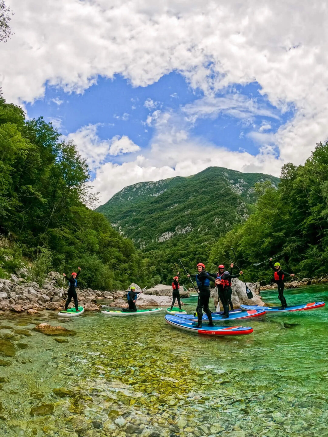 Stand-up paddleboard paddlers on a clear green river in a mountain valley under a cloudy sky