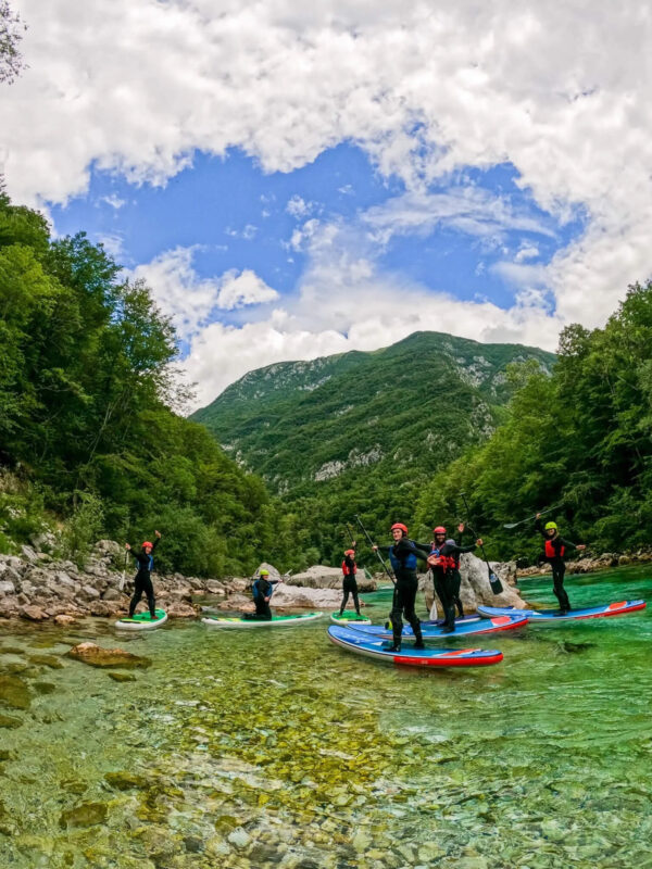 Stand-up paddleboard paddlers on a clear green river in a mountain valley under a cloudy sky