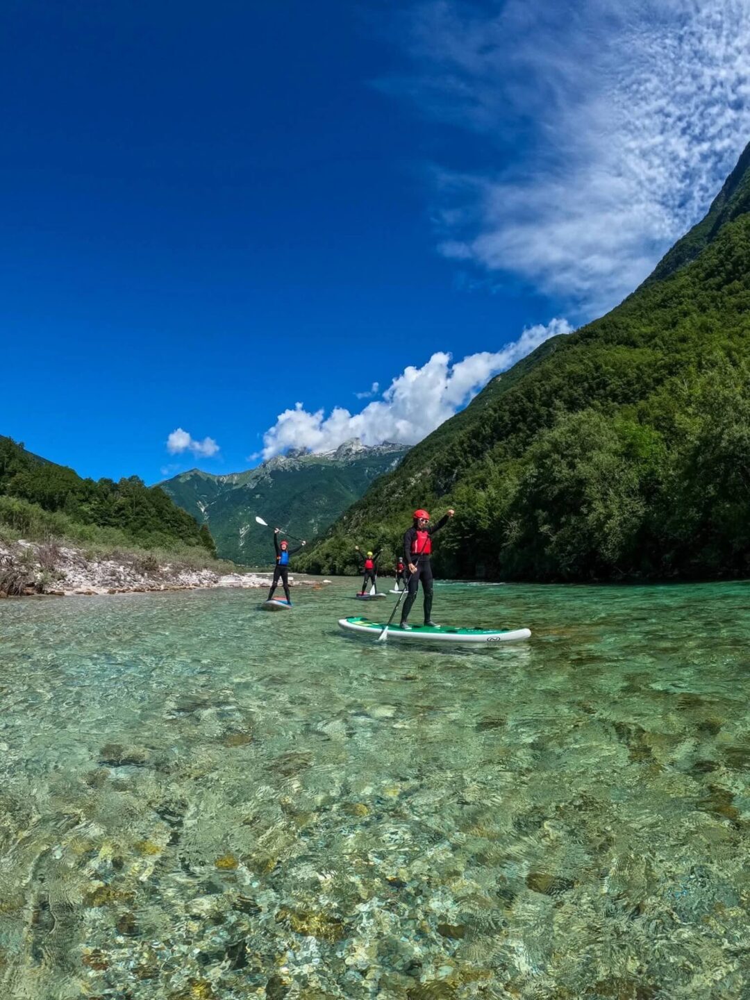Stand-up paddleboarding on a clear river with mountains in Slovenia, with paddlers on boards