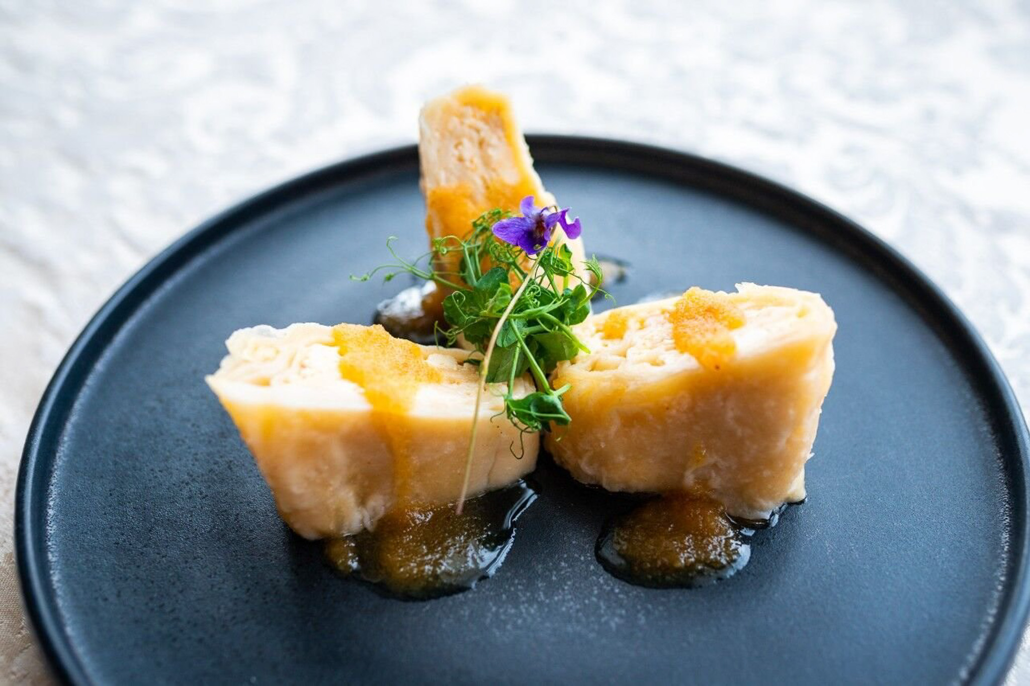 Plated cubes of food with edible flowers and microgreens on a dark plate