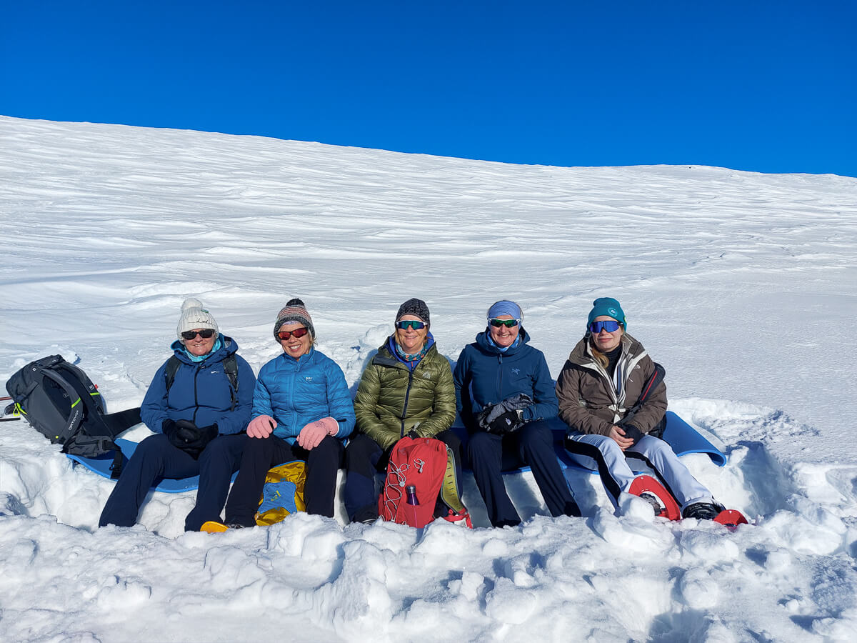 Women cross-country ski group posing in fresh snow under a bright blue sky