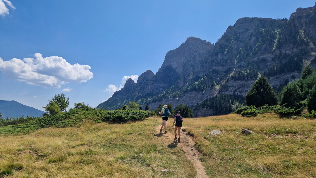 Women hiking on a mountain trail with Spanish Pyrenees peaks in the background.