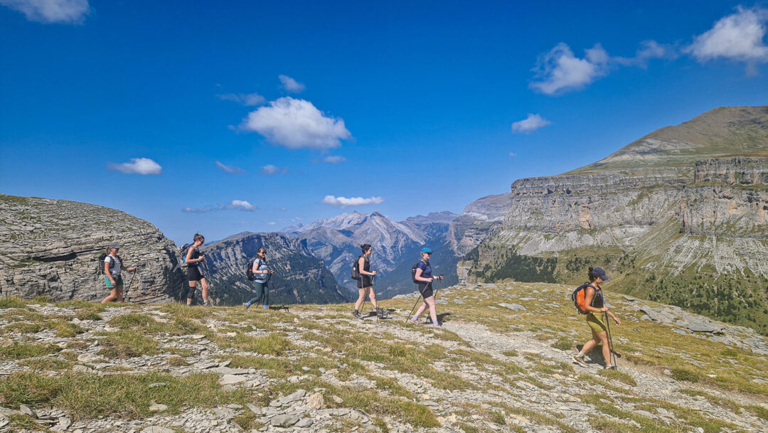 Women hiking on a mountain trail with panoramic views under a blue sky with clouds