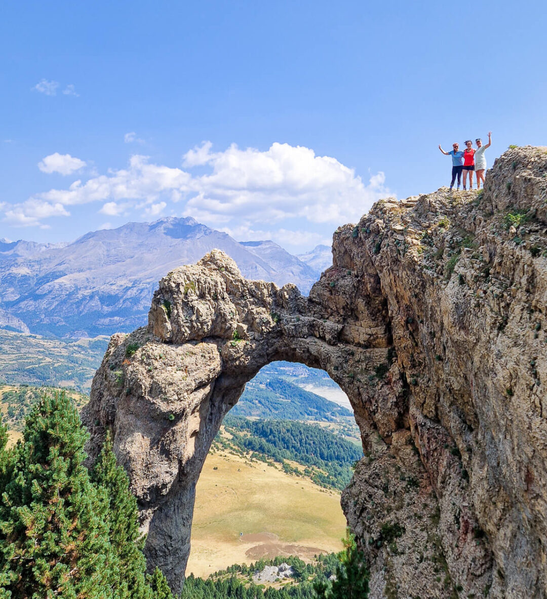 Hikers at a rocky viewpoint and natural arch, overlooking mountain valleys in the Pyrenees.