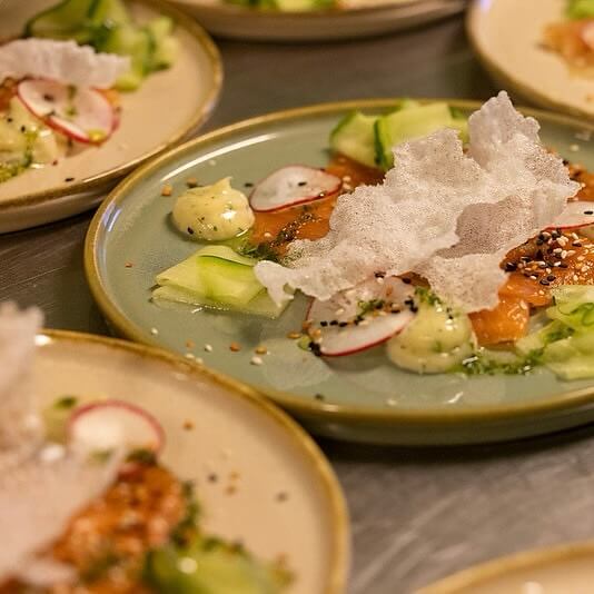 Plates of vegetable soup with sliced cucumber and radish, topped with crispy crackers, on a dining table