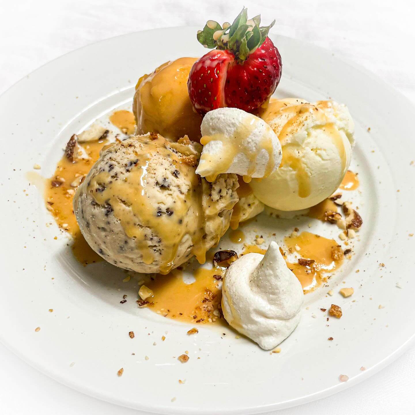 Dessert plate with ice cream, strawberries and meringue, topped with fruit and crushed nuts