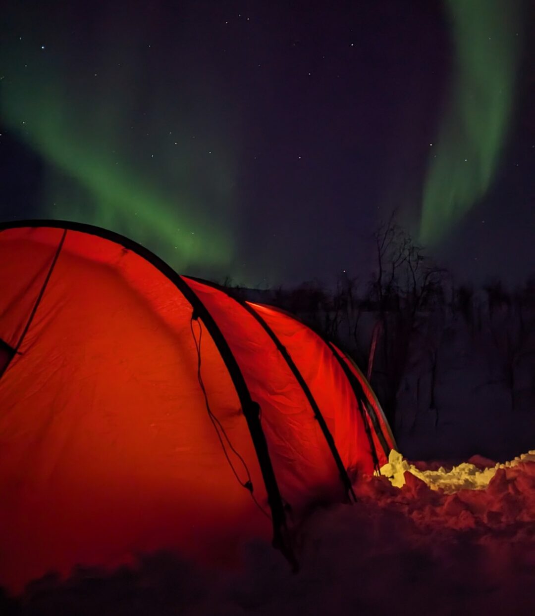 Red ski tent under northern lights on an Arctic hut-to-hut expedition at night in the far north
