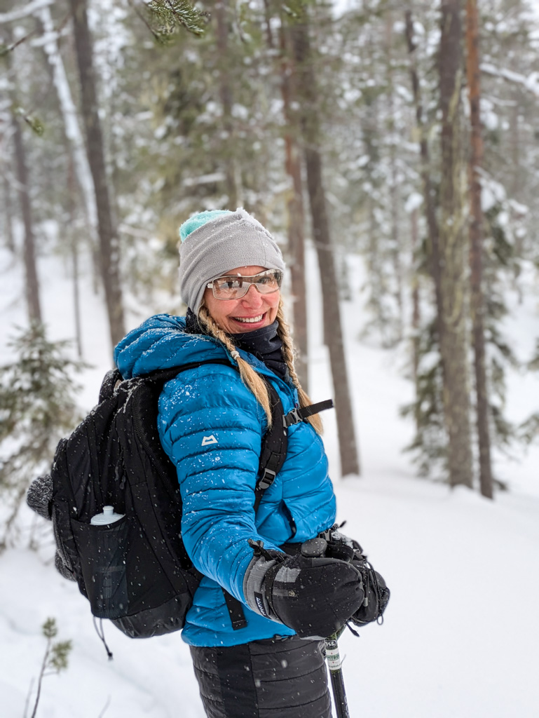 Women snowshoeing in a snowy forest, smiling in winter gear with backpack and trekking poles