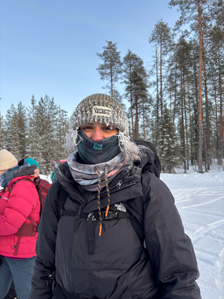 Woman in winter jacket and knitted hat reading “Ramsell Middle” in a snowy pine forest
