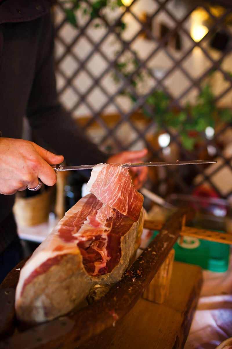 Hands carving cured ham at a mountain hut during a hut-to-hut hike