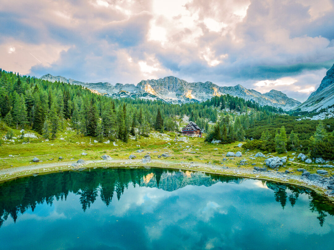 Alpine landscape with forest, mountain lake and a small wooden hut