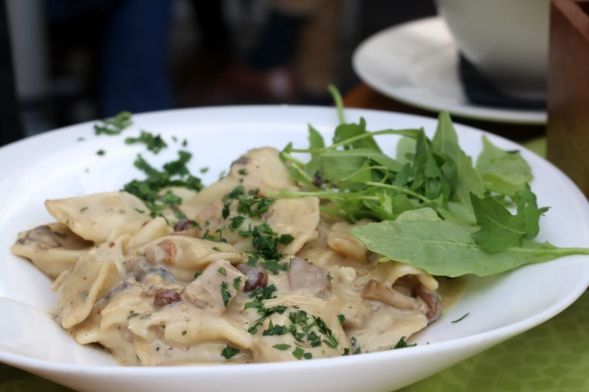 Creamy pasta dish topped with chopped herbs and fresh salad greens on a white plate