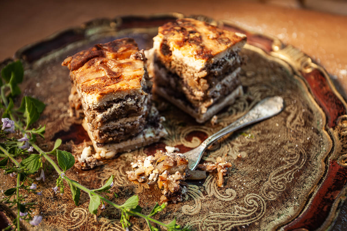 Slices of baked cake on an ornate plate with a spoon and fresh herbs nearby