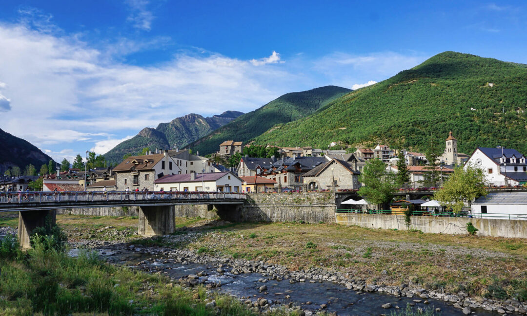 Hiking route along a river through a mountain village in the Spanish Pyrenees, with a stone bridge