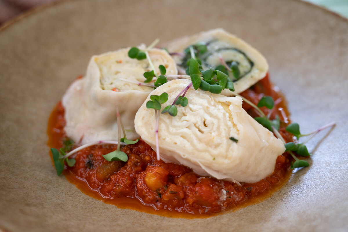 Creamy cheese and tomato sauce topped with microgreens on a plate, close-up.