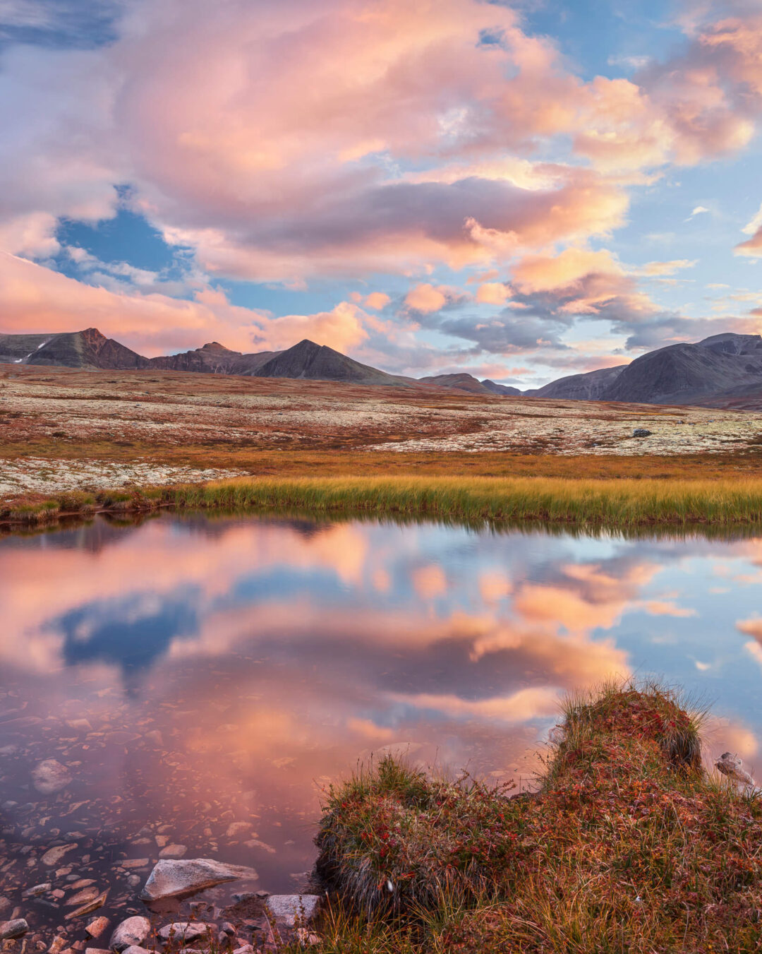 Mountain landscape at sunset with a reflective lake, valley, and rolling hills and peaks