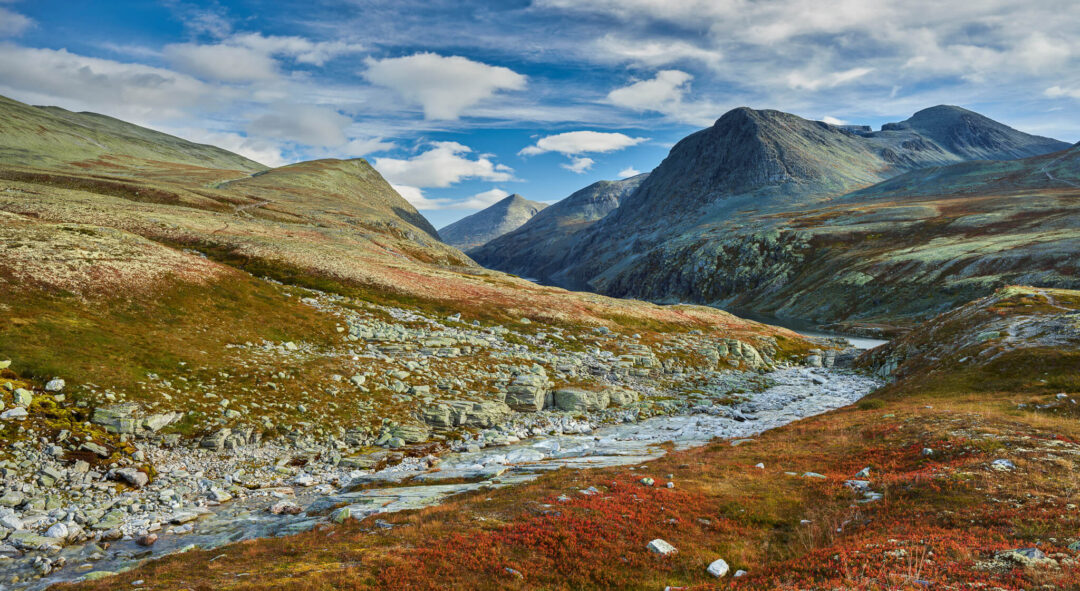 Mountain hiking valley with a winding river through rocky tundra under a cloudy sky