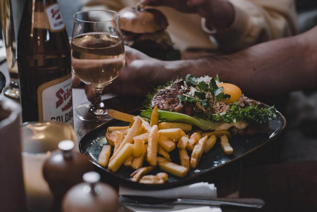 Two women dining together at a restaurant table with steak, chips and glasses of wine and beer